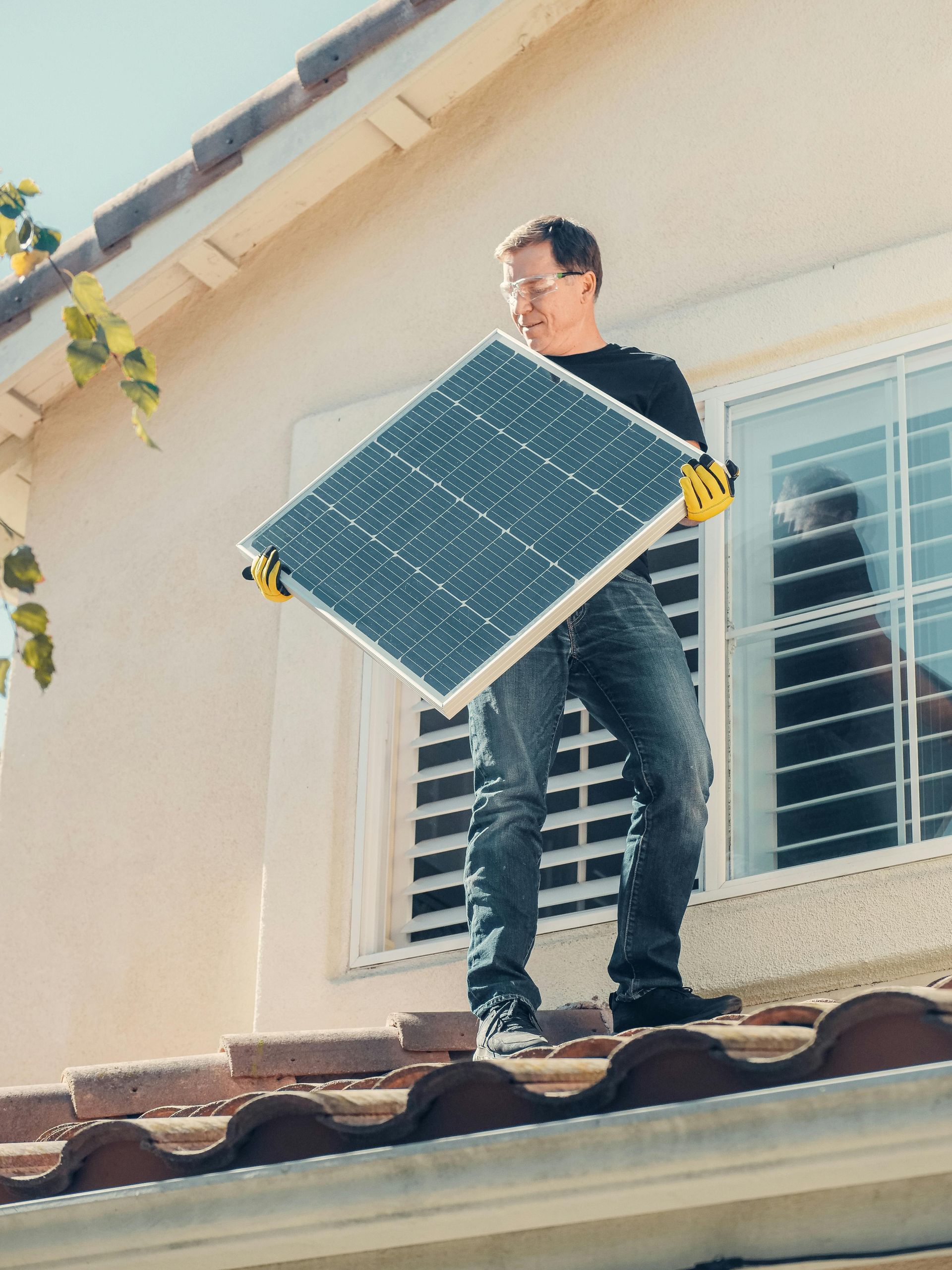 Ein Mann steht auf dem Dach eines Hauses und hält ein Solarpanel.